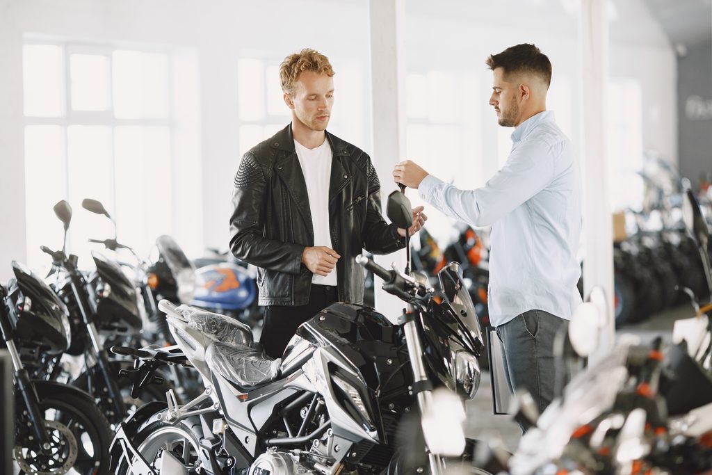 Homme qui vends une moto à un client en lui tendant les clés.